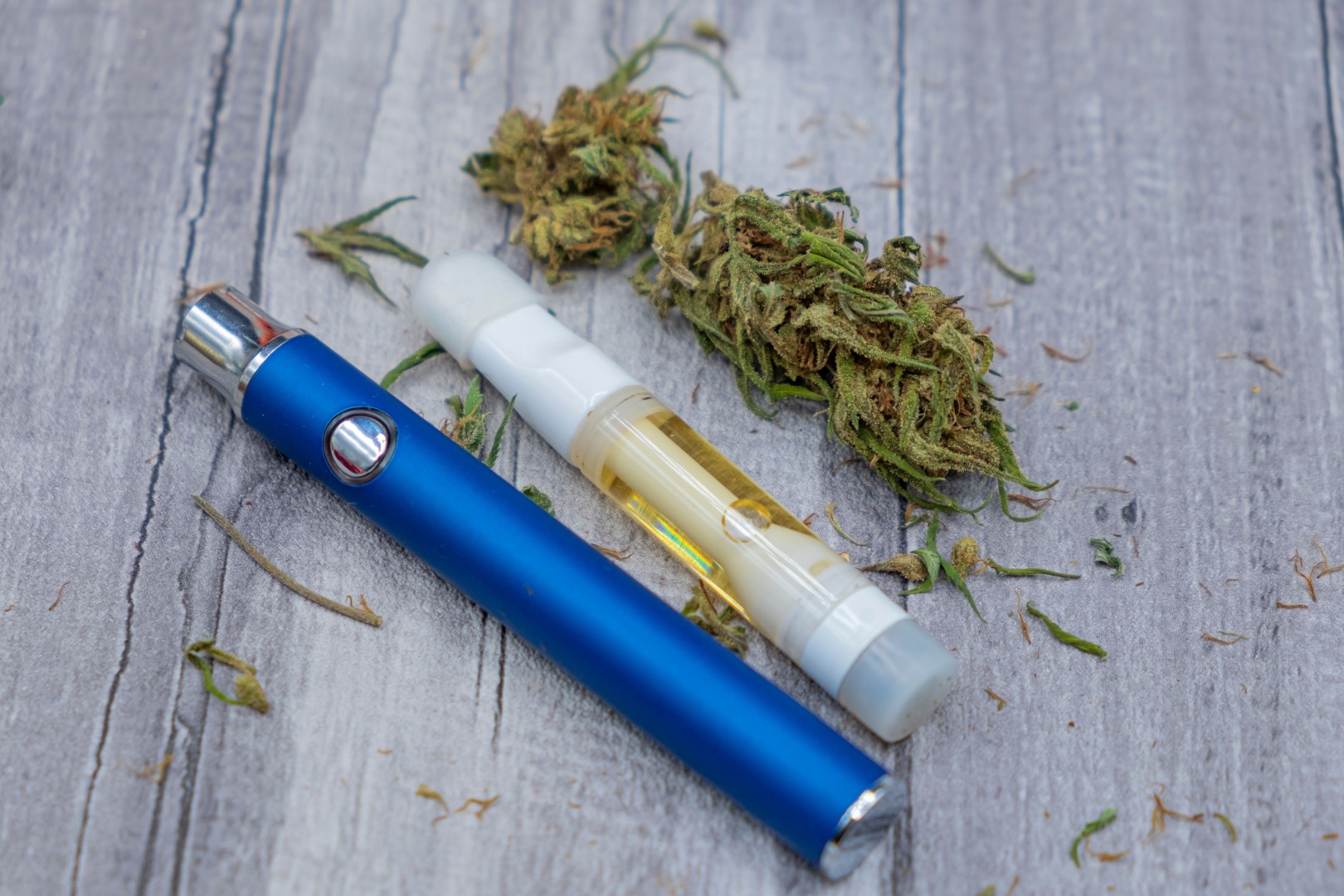 Home a blue vape 510 battery next to a pre filled cannabis concentrate cartridge and marijuana buds on a wooden background